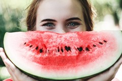 woman holding large slice of watermelon up to her face like a smile