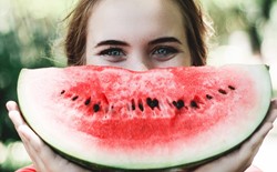 woman holding large slice of watermelon up to her face like a smile