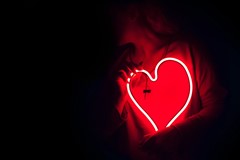red neon heart held by person on black background