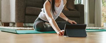 smiling woman sitting on yoga mat leans forward to use tablet
