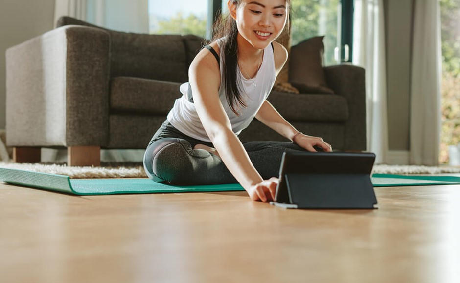 smiling woman sitting on yoga mat leans forward to use tablet