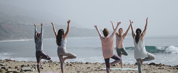 group of women in yoga tree pose on the beach on a cloudy day