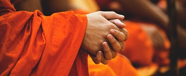 Buddhist monks in orange robes with clasped hands