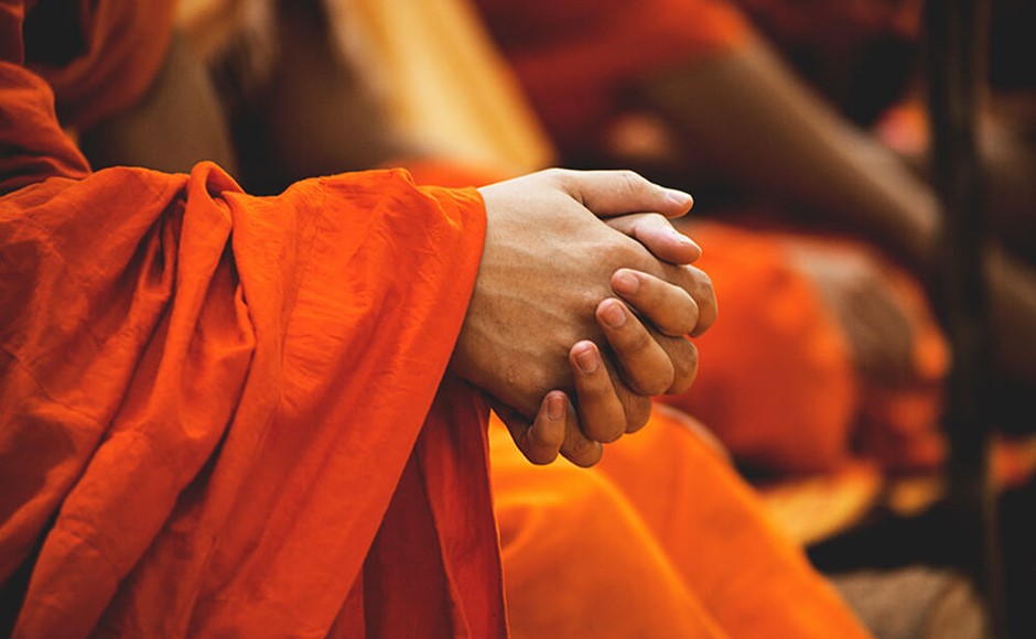 Buddhist monks in orange robes with clasped hands