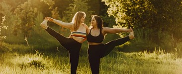 Two women with long hair doing yoga together in nature on a sunny day