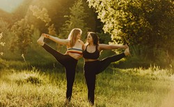 Two women with long hair doing yoga together in nature on a sunny day