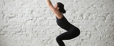 woman in black practicing Utkatasana chair pose with white background
